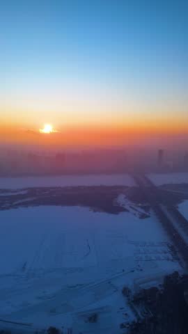 Vertical aerial drone shot of the Harbin City skyline with the frozen Songhua River at sunrise in Heilongjiang, China