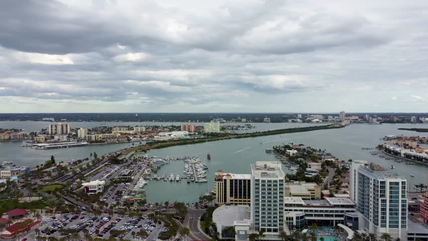 Aerial view of Clearwater Beach, Florida, featuring luxury resorts, marina, Clearwater Bridge, Mandalay Ave roundabout, Coronado Dr, parking, restaurants, fishing charters, and pirate cruise.