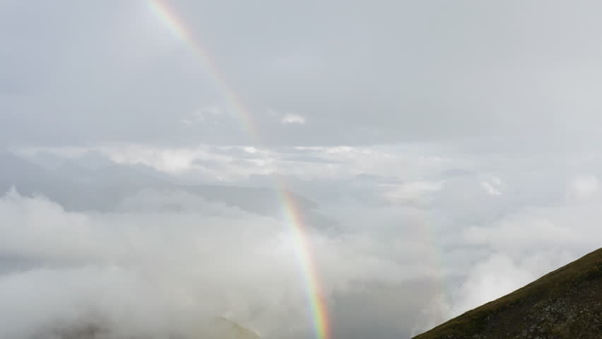 Colorful rainbow behind a mountain, surrounded by clouds and foggy weather, high above the Glacier, copy space, bokeh shot