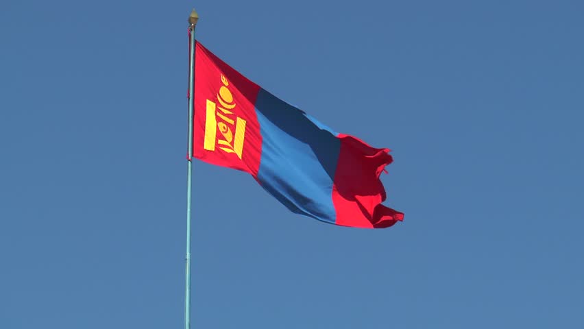 The Mongolian national flag flutters in the wind against a cloudless blue sky on a sunny summer day.