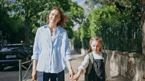 Mother daughter walking sunshine alley closeup. Cute schoolgirl strolling with mom at sunny street. Little child with backpack going calmly after lessons talking parent. Small kid holding woman hand - Powered by Shutterstock - Get 15% off with code: PIKWIZARD15