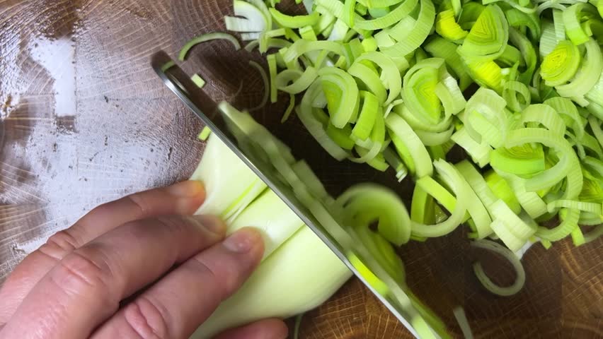 Chef chops leek stems with a cleaver on wooden cutting board.