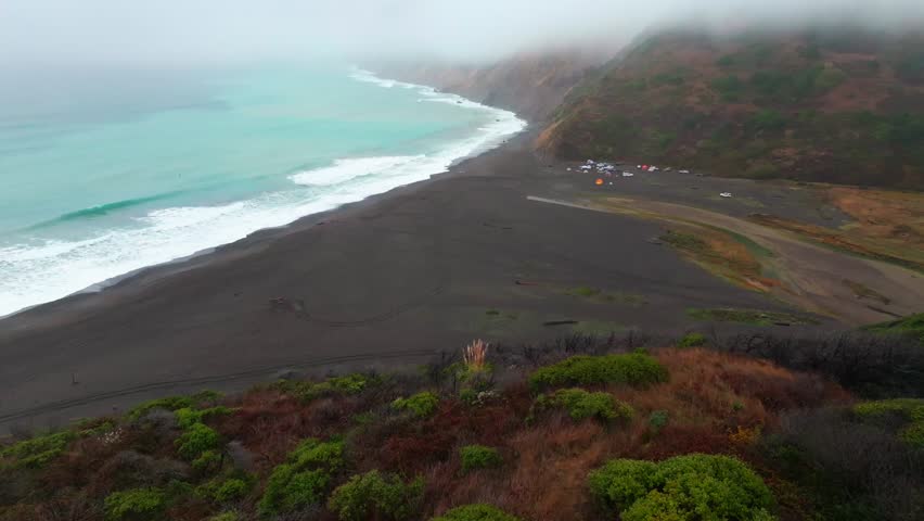 Waves black sand 4wd tents rugged coastline USAL Beach Campground Lost Coast Trail California aerial drone fog mist rain cloudy morning Pacific Ocean PNW Nor Cali mountainside forward pan up motion