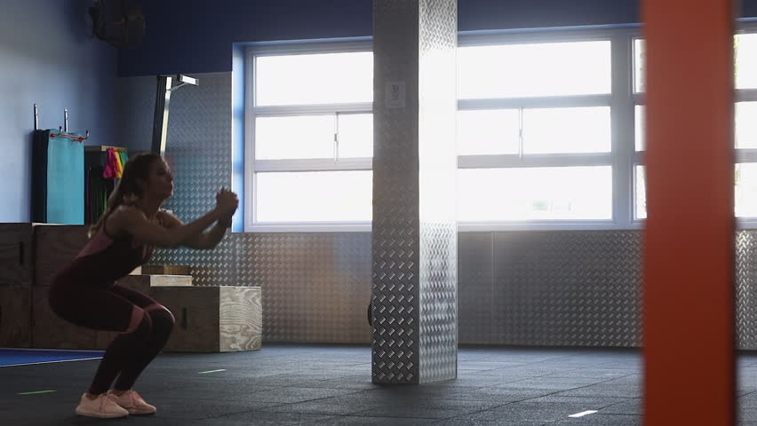 Panning across female fitness model in gym demonstrating jump squats