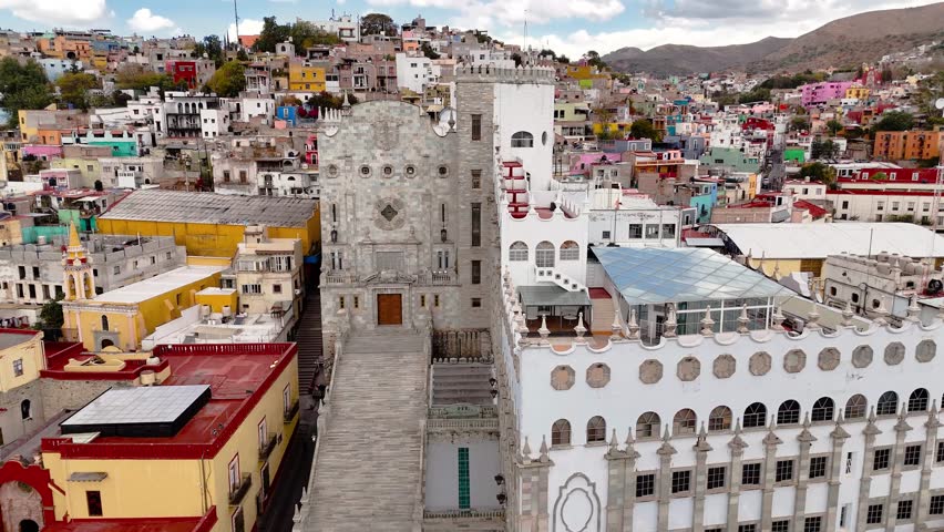 Facade of the university in the city of Guanajuato, Mexico. Drone camera hovers in front of the building and shows colorful houses in the background