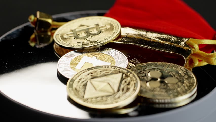 Physical coins of Bitcoin, Ripple, Litecoin, and Ethereum rotate on a mirror surface, spilled from a small red storage bag