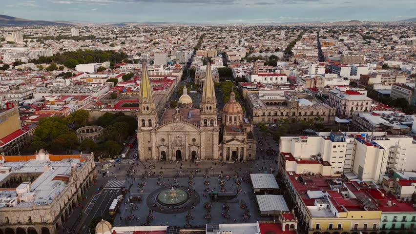 Guadalajara, Mexico - January 12, 2025: Hundreds of tourists stroll through the main squares of the historic downtown. Drone camera orbits around the cathedral and other historic buildings