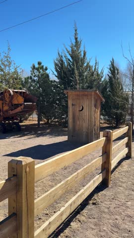 Rustic wooden outhouse near old farmhouse in rural countryside setting, vertical