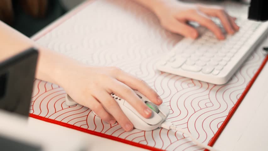 Hands are on white gaming keyboard and mouse in cozy desk setup. Minimalistic design and focus on gaming peripherals create atmosphere of comfort and productivity for gaming enthusiasts.