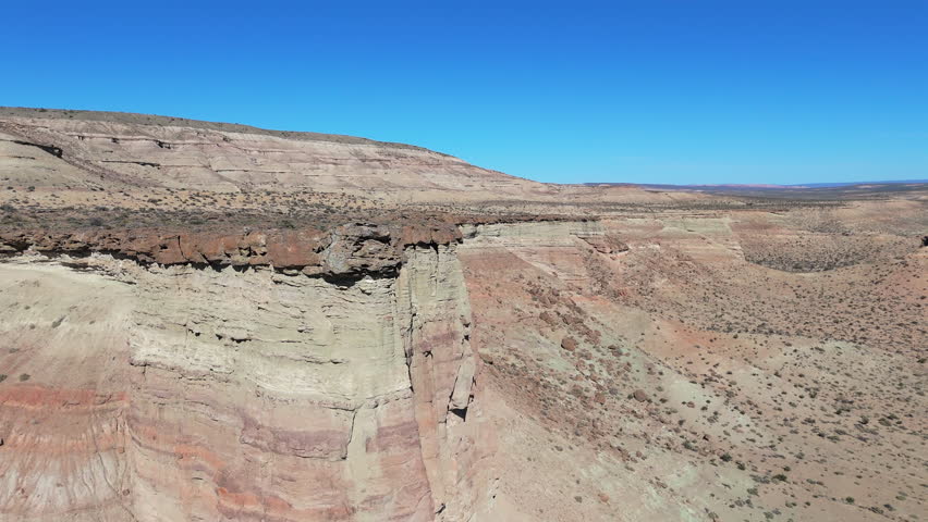 Aerial view of the rugged Patagonian landscape along Route 45 in Argentina, showcasing colorful rock formations, dramatic cliffs, and the vast expanse of the desert terrain under blue sky, drone orbit
