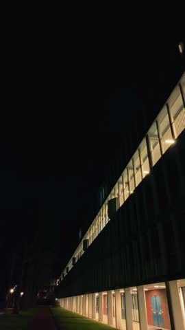 Modern student housing complex in Amsterdam Noord lit up at night, with bright interior lights creating stark contrast against dark sky. Scene of urban living and contemporary design in Netherlands