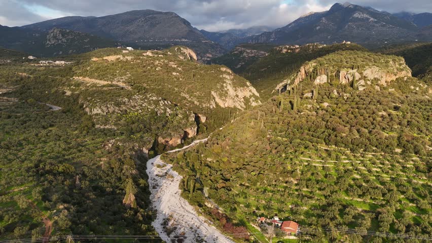 A breathtaking aerial view of Viros Gorge near Kardamyli, Greece, captured during sunset. The golden light enhances the rugged cliffs, deep canyon, and surrounding Taygetos Mountains.