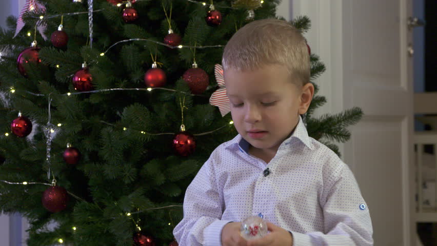 Happy child holding snow globe with figurine of Santa Claus. Smiling face of little boy near Christmas tree. Merry Christmas and Happy New year winter holidays.