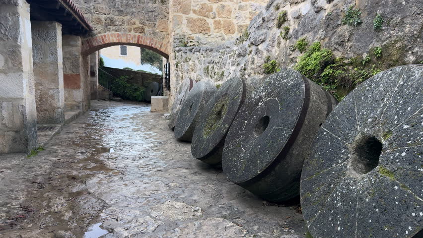 Woman in grey coat walking past old grinding stones used in watermill in Krka National Park, Croatia