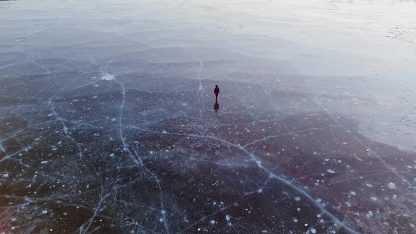 Silhouette of person strolling on ice surface, frozen lake shining with sunset light