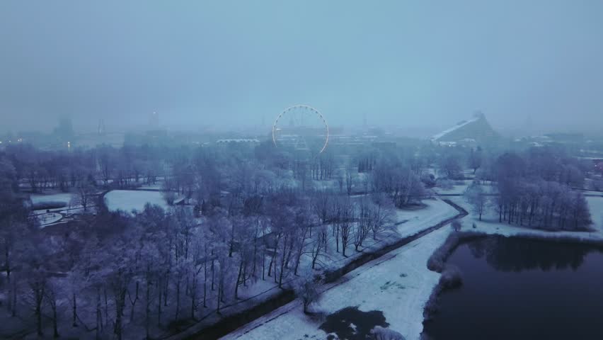 Riga winter park in snow, Ferris wheel peeking through the fog, early morning