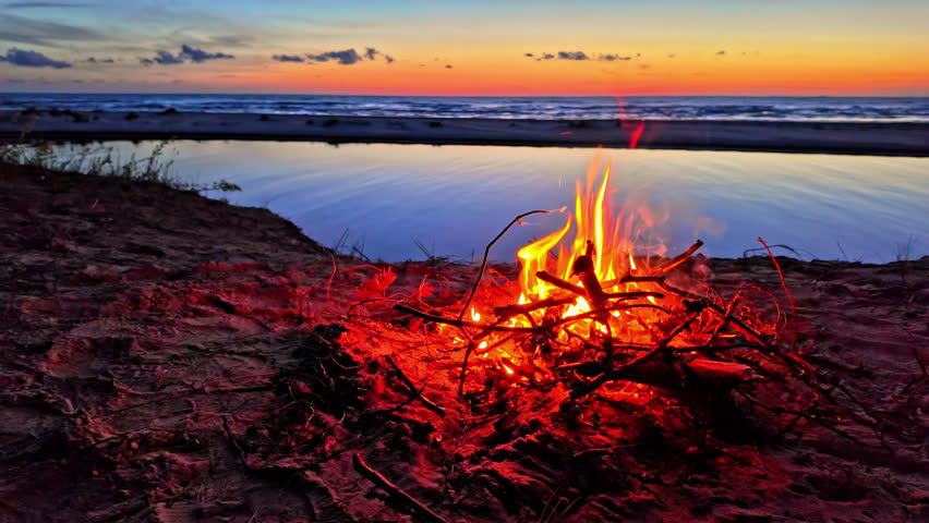 Colorful fireplace on the beach at sunset, camping feeling with warm fire, ocean, sea in the back, zoom in