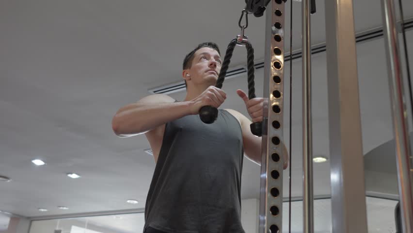 A man working out in the gym using a cable machine, focusing on upper-body strength training. Concept of fitness, health, and physical activity.
