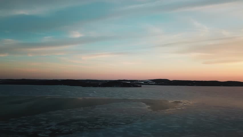 Aerial view of a frozen lake in Wisconsin at sunset, featuring vibrant orange hues and a peaceful, serene atmosphere.