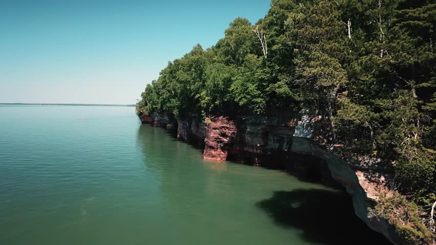 A breathtaking view of the Apostle Islands with vibrant green forested cliffs reflecting in the clear waters of Lake Superior.