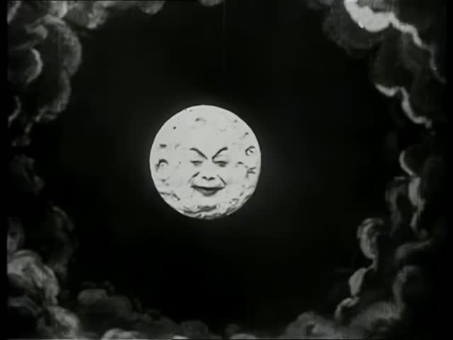 A Trip to the Moon, Le Voyage dans la lune (1902). Vintage video still of a full moon with a face, surrounded by clouds. Shot from a low angle, evoking early 20th-century film style.