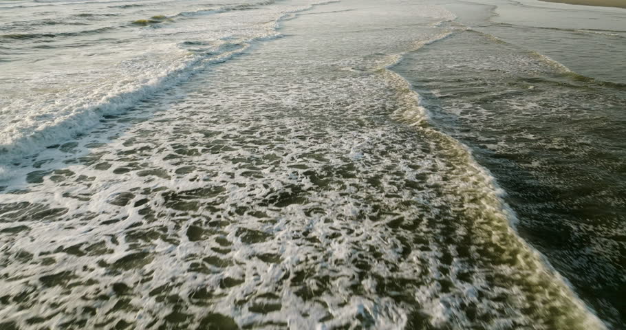 Aerial dolly perpendicular to open ocean waves crashing as whitewash spreads rolling to beach, natural background