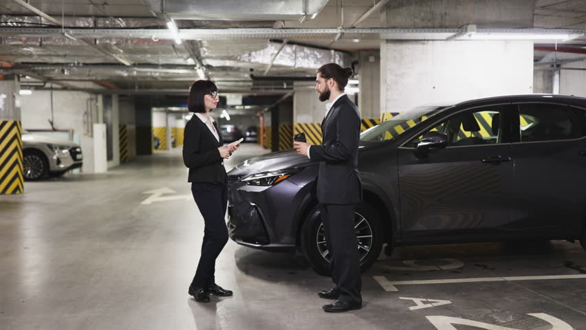 Caucasian businessman and businesswoman in formal attire shaking hands in underground car park. Professional meeting in urban setting conveying cooperation, agreement, successful partnership.