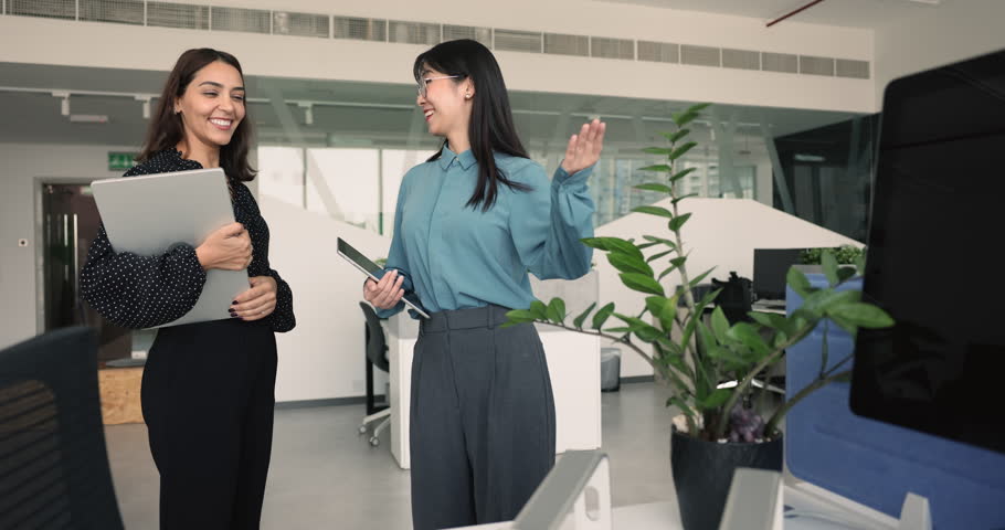 Personnel manager showing office workplace to newly hired employee woman, pointing at desk with computer, speaking, smiling. Inspector checking work condition in company workspace
