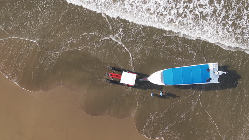 An aerial view captures a vibrant yellow tractor, energetically towing a boat towards the surf in beautiful Costa Rica, vividly illustrating the lively essence of tropical maritime life