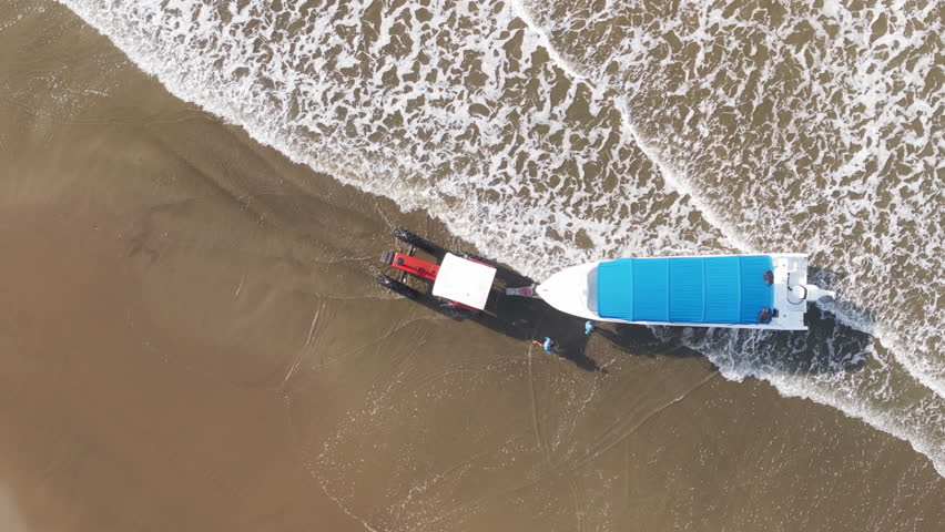 An aerial view captures a vibrant yellow tractor, energetically towing a boat towards the surf in beautiful Costa Rica, vividly illustrating the lively essence of tropical maritime life