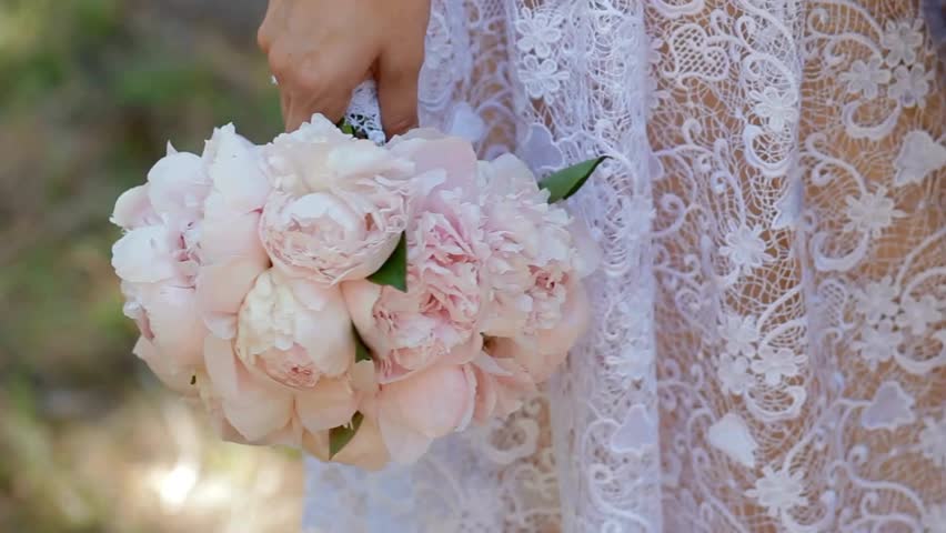 Beautiful wedding bouquet held by bride in lace dress during outdoor ceremony in a serene garden setting