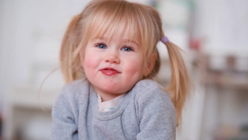 A little child girl of Caucasian appearance, blonde, smiles and grimaces in front of the camera.