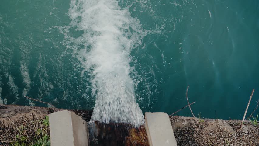 Water flows from a concrete pipe into a reservoir. The water is a beautiful turquoise color and creates a white, frothy stream as it enters the reservoir. water management, irrigation, environment.