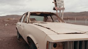 Abandoned car in the desert near a last stop sign with mountains in the background. The car is rusted and broken with no windows left, giving a sense of desolation and abandonment in a vast, - Powered by Shutterstock - Get 15% off with code: PIKWIZARD15