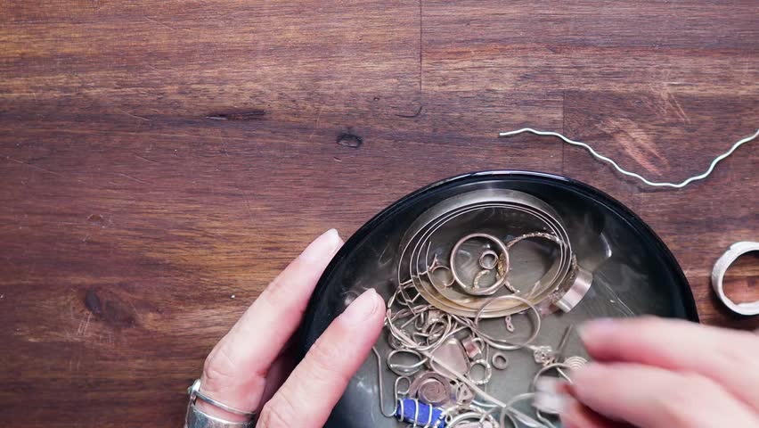 Close-up of searching through a small bowl of silver scraps, picking out pieces for metalwork. Ideal for jewelry making, recycling, and craftsmanship content.