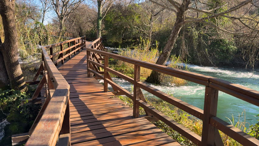 Beautiful woman in grey coat walking over a wooden bridge in Krka National Park, Croatia