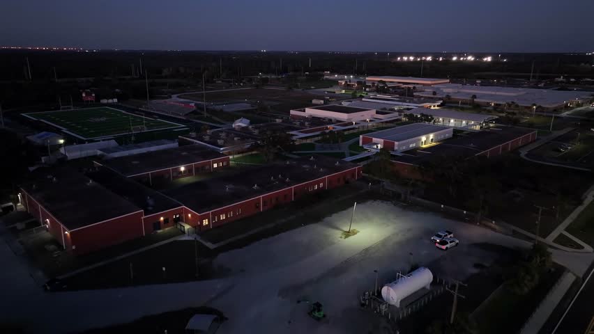 Red buildings of Eisenhower Middle School campus at night. Football Field in Apollo Beach, big Bend, Florida. Aerial approaching shot.