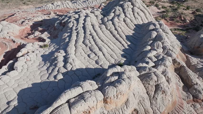 A drone flying backwards and panning up to reveal the unique sandstone features of White Pocket Arizona surrounded by the sandy desert of the Vermillion Cliffs at midday