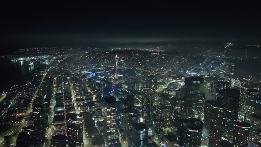 Nighttime establishing cityscape of the Emerald City. Seattle skyscrapers, streets, and landmarks illuminated in scenic high-angle view of iconic West Coast city.