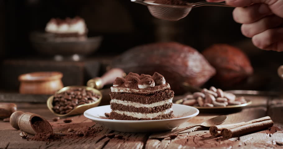 Close-up shot of a male baker's hands carefully preparing a homemade tiramisu cake. Hands gently sprinkle cocoa powder over the creamy mascarpone layer.
