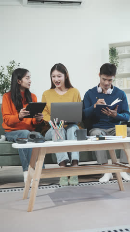 Three Asian young adult students sit in university living room, discussing their study abroad experiences, academic research, preparing thesis report, planning future global education opportunities.