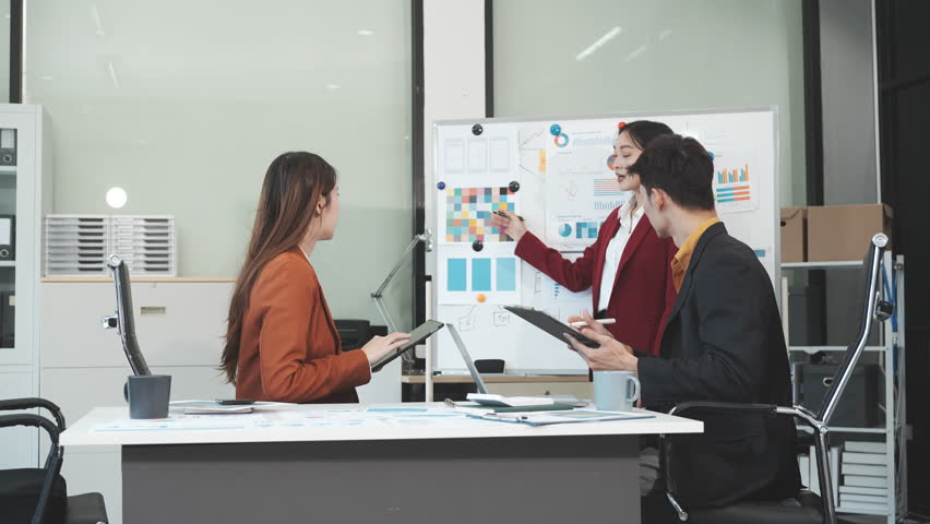 Three Asian business professionals gather in boardroom for annual meeting, discussing strategic goals, future projections while proposing ideas, engaging in decision-making for corporate growth.