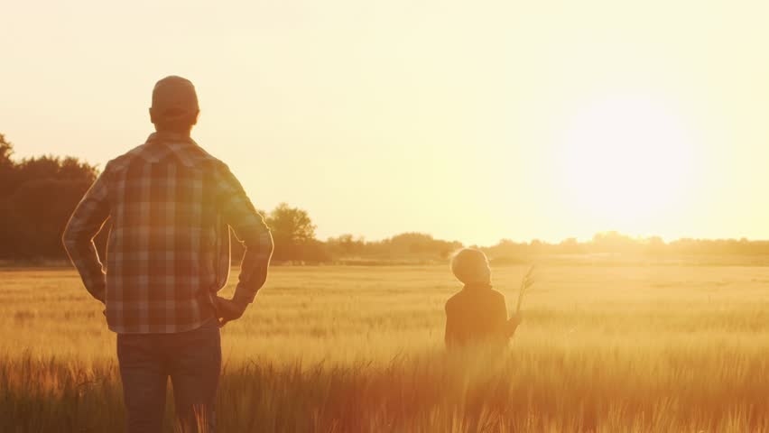 Farmer and his son in front of a sunset agricultural landscape. Man and a boy in a countryside field. Fatherhood, country life, farming and country lifestyle concept.