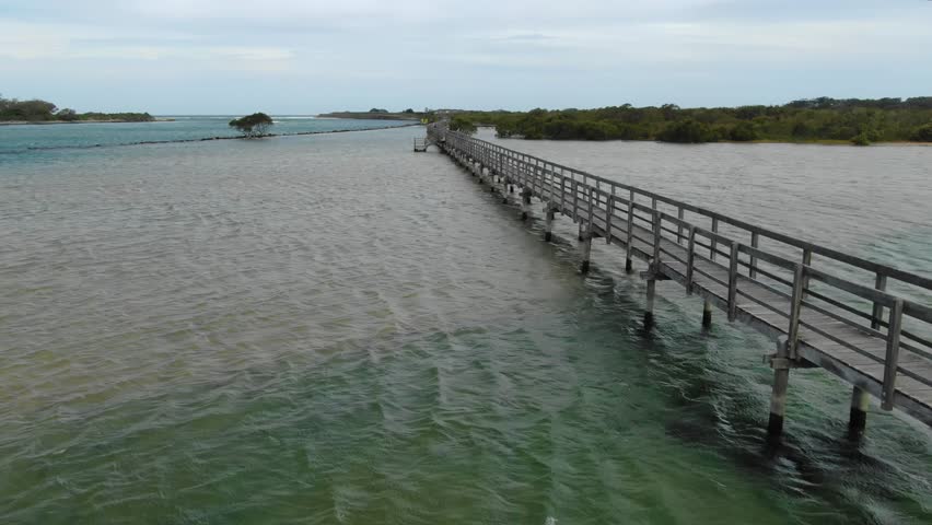 Urunga Boardwalk, wooden footbridge over Bellinger River, lagoon, Urunga, New South Wales, Australia. Aerial drone flying at low altitude along walkway
