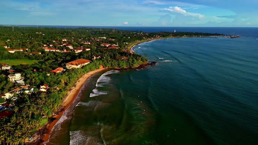 Drone aerial landscape of surfers riding ocean waves at Madiha beach break coastline headland with resort hotels town village Matara Sri Lanka Asia travel tourism surfing holidays