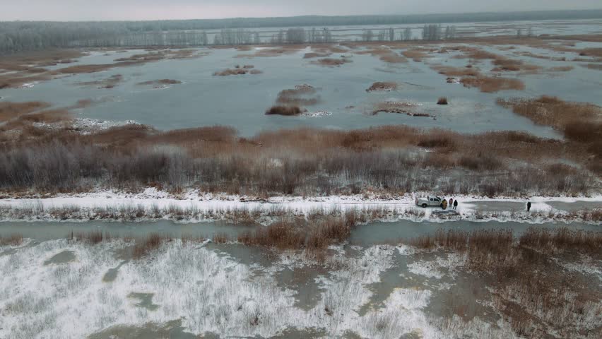 Aerial view of a frozen marshland with patches of ice, brown vegetation, and misty surroundings, creating a cold and desolate winter landscape.