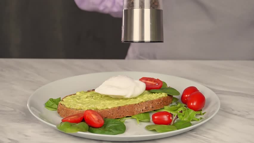 A woman with an electric mill prepares savory toasts with avocado, poached egg
