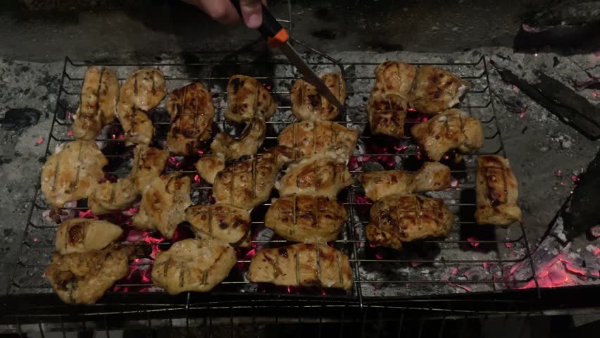 Chicken meat is grilled on the grill, charcoal burns in the brazier