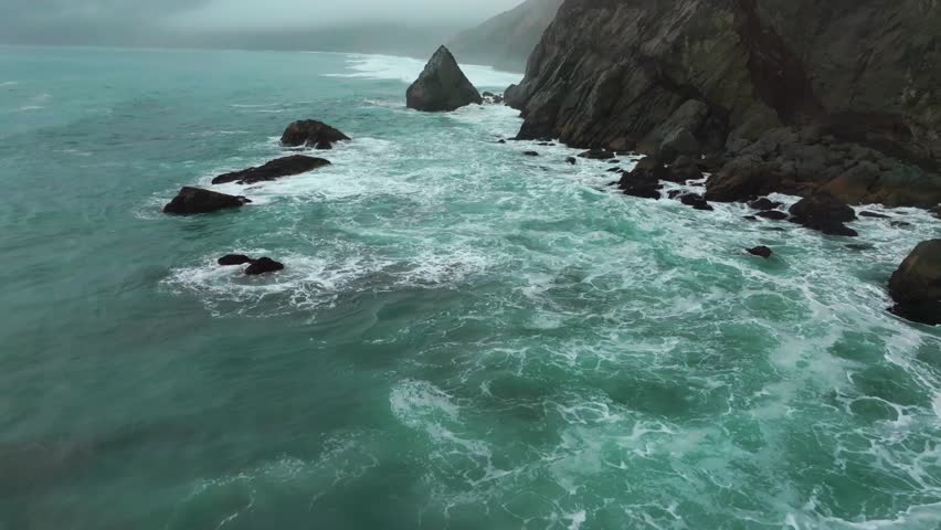 Waves crashing boulder rocks rugged coastline black sand USAL Beach Campground Lost Coast Trail California aerial drone fog mist rain cloudy layers mountainside morning Pacific Ocean forward pan up