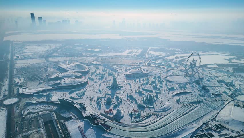 Aerial view of the Harbin Ice Festival 2025, showcasing intricate ice sculptures, frozen palaces, and a vast winter wonderland set against the city skyline under clear blue skies. China